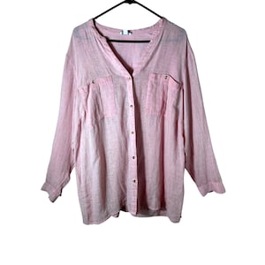 May include: A light pink long-sleeve shirt with a V-neck collar and two front pockets. The shirt has a button-down closure and is hanging on a black hanger. The fabric appears to be a lightweight linen or linen blend.