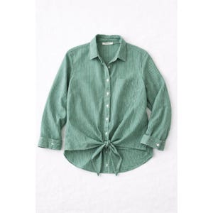 Puede incluir: Camisa abotonada a rayas verdes y blancas con mangas largas. La camisa tiene un cierre de lazo en la cintura y un bolsillo en el pecho. La tela tiene una apariencia texturizada.