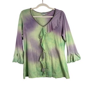 May include: A long-sleeved tie-dye top in shades of green and purple, hanging on a white hanger. The top features a V-neckline with a ruffled trim down the front and at the cuffs of the sleeves. The fabric appears soft and lightweight.