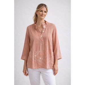 May include: A peach-colored, striped tunic with a mandarin collar and three-quarter sleeves. The top features a button-down placket and two front pockets with button details. The model is wearing white pants.