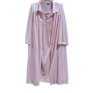 May include: A light pink satin robe and nightgown set. The robe has a collared neckline, long sleeves, and a button-down front. The nightgown is visible underneath, with a scoop neckline and lace detailing. The set is made of a soft, flowing fabric.