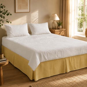 May include: A bed featuring a white linen duvet cover and two matching white pillows, paired with a solid mustard yellow bed skirt that covers the base. The bedding set provides a clean, neutral look with a textured fabric finish on the top layer.