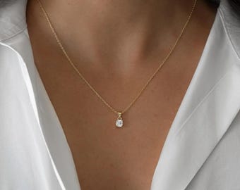 Può includere: Una delicata collana d'oro con un piccolo pendente a forma di diamante a taglio quadrato. Il pendente è sospeso a una sottile catena d'oro. La collana è indossata su una camicia bianca.