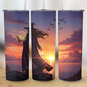 May include: A tumbler depicting a witch with a book and lantern, set against a sunset sky with bats. The witch is wearing a purple robe and hat. The background includes the ocean and clouds. The tumbler is cylindrical and has a straw.