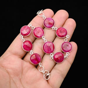 Op de afbeelding: Een zilveren armband met grote, ronde, robijnkleurige edelstenen. De edelstenen zijn gezet in individuele zilveren zettingen en verbonden met kleine zilveren connectoren. De armband wordt getoond tegen een zwarte achtergrond.