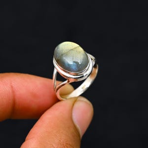 Può includere: Anello in argento con una pietra di labradorite ovale e iridescente. La pietra mostra una miscela di tonalità blu, verdi e gialle. L'anello ha un design a gambo diviso e una finitura lucida. La gemma misura circa 1,9 cm di lunghezza.