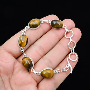 May include: A silver bracelet featuring oval-shaped tiger's eye gemstones. The gemstones are a mix of brown and gold hues, set in a silver metal. The bracelet has a toggle clasp for closure.