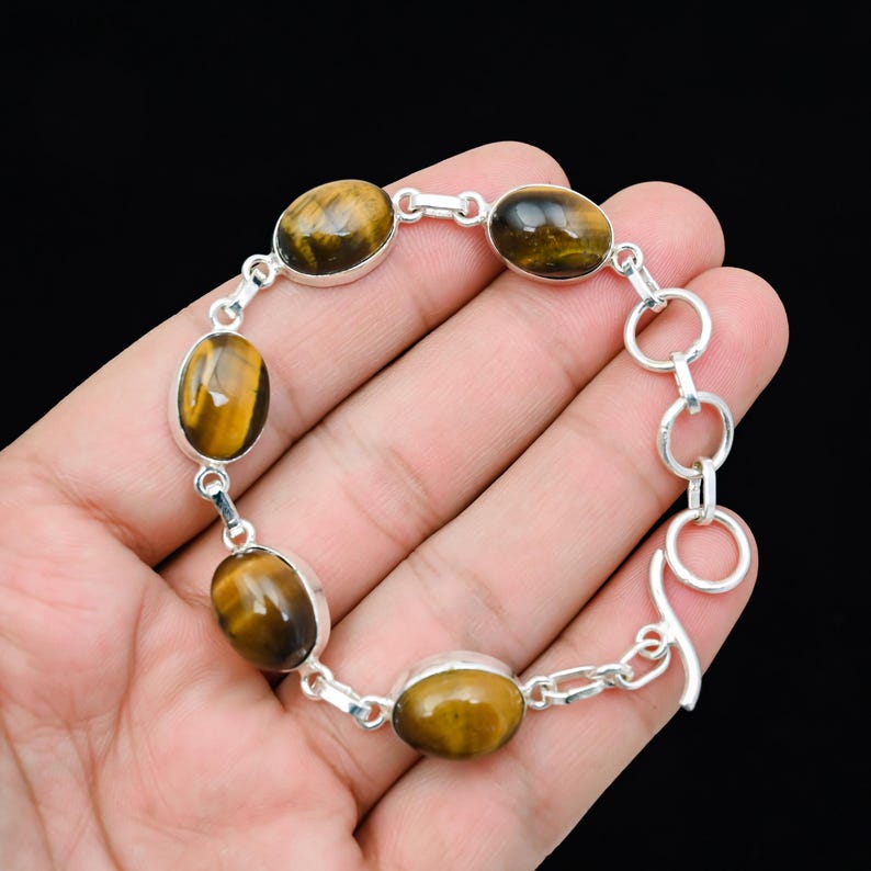 May include: A silver bracelet featuring oval-shaped tiger's eye gemstones. The gemstones are a mix of brown and gold hues, set in a silver metal. The bracelet has a toggle clasp for closure.
