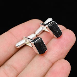 May include: A pair of silver cufflinks featuring rectangular black tourmaline stones. The cufflinks have a polished silver finish and a classic design, suitable for formal wear or adding a touch of elegance to any outfit.
