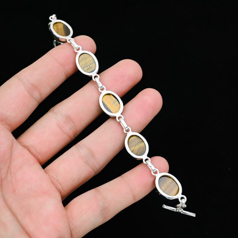 May include: Silver bracelet featuring oval-shaped tiger's eye stones. The stones are set in a silver metal frame and connected by small silver links. The bracelet has a toggle clasp.