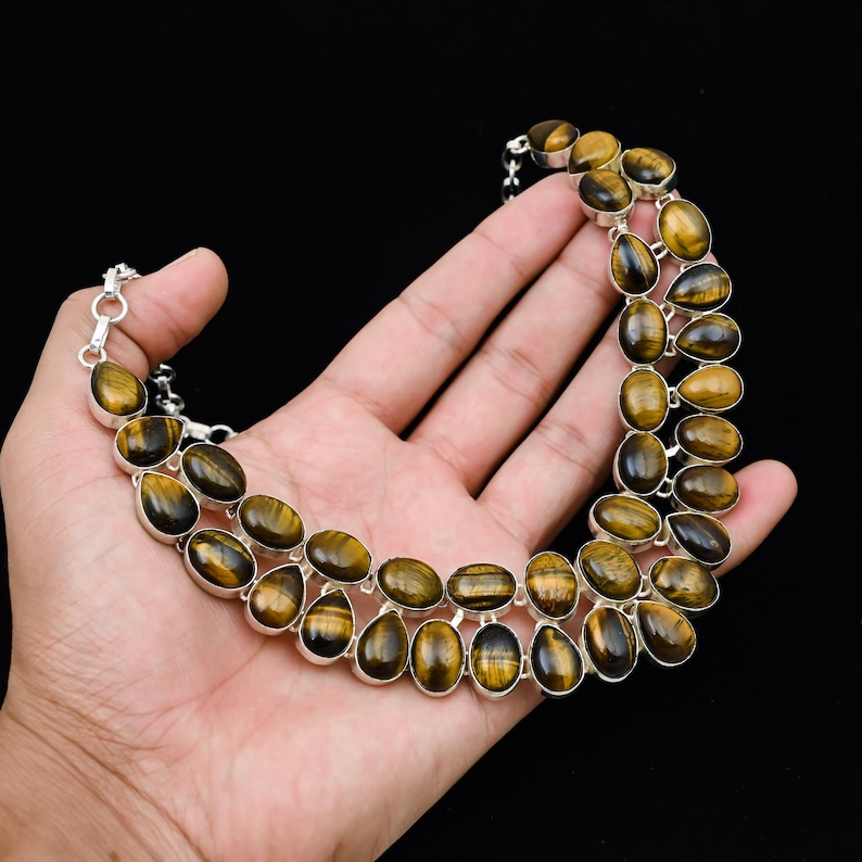 May include: A two-strand necklace featuring oval and teardrop-shaped tiger's eye stones set in silver. The stones have a warm, golden-brown color with dark brown stripes. The necklace is displayed against a black background.