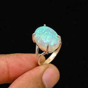 May include: A silver ring featuring a large, oval opal gemstone. The opal displays a vibrant play of color with shades of blue and green. The ring's setting has a classic design, with the gemstone held securely by four prongs.