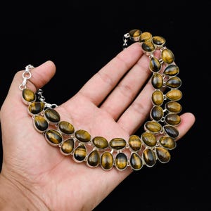 May include: A two-strand necklace featuring oval and teardrop-shaped tiger's eye stones set in silver. The stones have a warm, golden-brown color with dark brown stripes. The necklace is displayed against a black background.