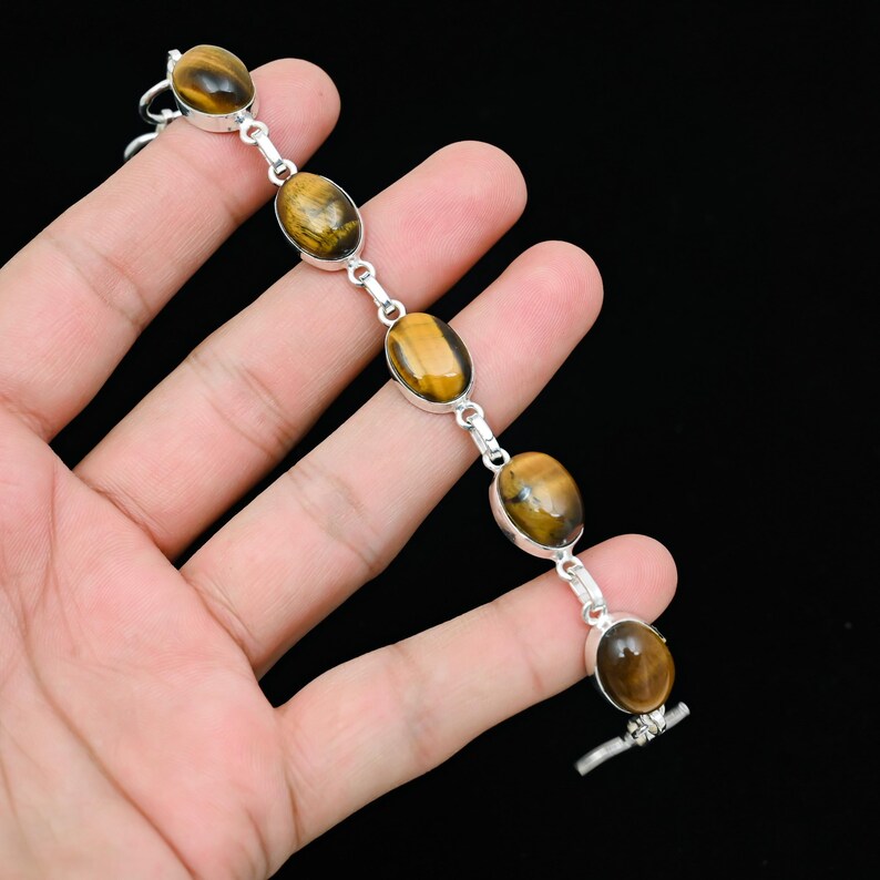 May include: A silver bracelet featuring oval tiger's eye gemstones. The gemstones are a warm brown color with golden streaks. The bracelet is connected by silver links and has a toggle clasp. The bracelet is approximately 7 inches long.