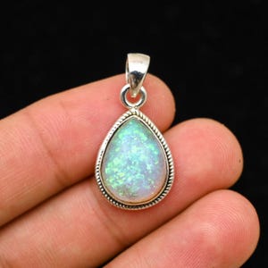 Peut inclure: Pendentif en argent en forme de goutte d'eau avec une opale aux reflets irisés verts et bleus. Le bijou est bordé d'un motif torsadé et possède une petite bélière pour une chaîne. Mesure environ 2.5 cm de long.