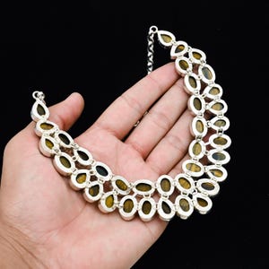May include: A silver-toned necklace with oval-shaped, tiger's eye gemstones. The gemstones are set in a double-strand design, with a chain clasp. The necklace is displayed against a black background.
