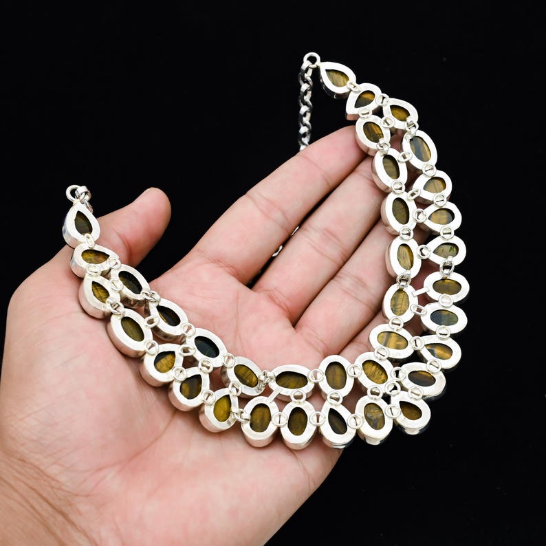 May include: A silver-toned necklace with oval-shaped, tiger's eye gemstones. The gemstones are set in a double-strand design, with a chain clasp. The necklace is displayed against a black background.