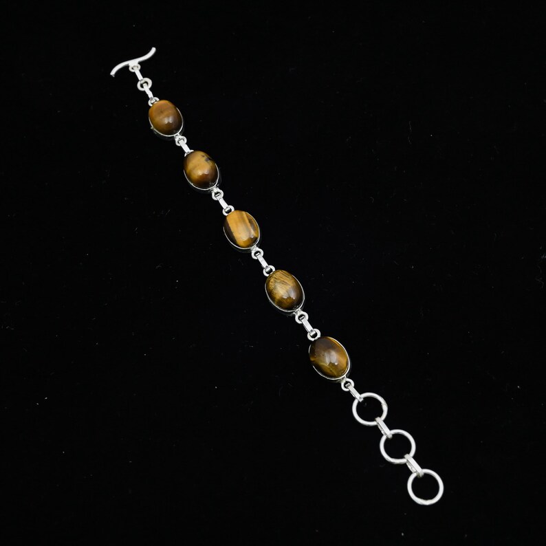 May include: A silver bracelet featuring oval tiger's eye stones. The stones are set in individual silver settings and connected by small silver links. The bracelet has a toggle clasp and three adjustable rings for sizing. The tiger's eye stones have a warm brown color.