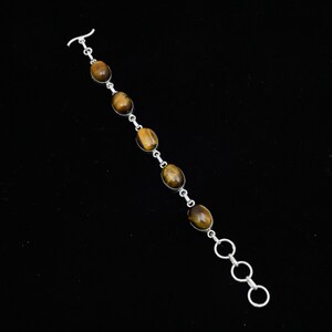 May include: A silver bracelet featuring oval tiger's eye stones. The stones are set in individual silver settings and connected by small silver links. The bracelet has a toggle clasp and three adjustable rings for sizing. The tiger's eye stones have a warm brown color.