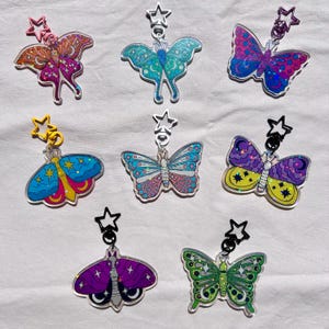 Puede incluir: Siete llaveros con forma de mariposa con cierres en forma de estrella. Los llaveros presentan varios diseños, incluidos patrones celestiales, y una gama de colores como rosa, azul, verde y morado. Cada llavero está hecho de acrílico transparente.