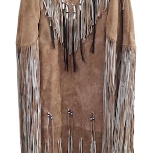 May include: Brown suede dress with long fringe detailing. The dress features a decorative circular emblem with a blue, black, and yellow design. White and black beaded accents are present along the neckline and hem.