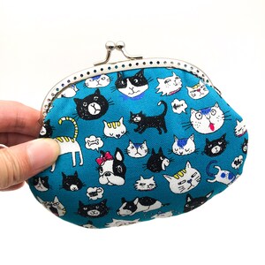 Puede incluir: Una cartera de monedas azul con un cierre plateado y un estampado colorido de gatos y perros. El estampado presenta varias razas de gatos y perros en diferentes poses.
