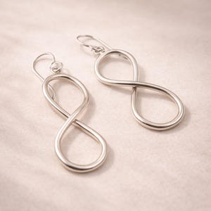 Peut inclure: Une paire de boucles d'oreilles argentées en forme de symbole infini. Les boucles d'oreilles sont en métal lisse et brillant et présentent un design simple et élégant. Le symbole de l'infini est une boucle continue, et les boucles d'oreilles ont une fermeture à crochet.