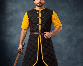 May include: A black quilted gambeson with yellow trim and short sleeves, featuring a front opening secured by four metal buckles and a brown leather belt at the waist. The garment has a diamond-stitched pattern and reaches down to the mid-thigh.