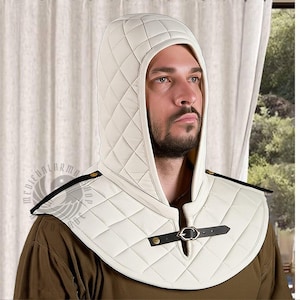 May include: Cream-colored quilted hood and shoulder piece with black leather accents. The hood features a diamond pattern and a leather strap with a metal buckle closure. The shoulder piece has black leather straps with gold-colored rivets.