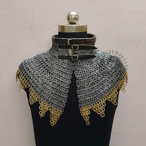 Peut inclure: Un collier de mailles avec un tour de cou en cuir et une fermeture à boucle. Le collier est fait d'anneaux métalliques argentés avec une bordure dorée sur le bord inférieur. Le collier est présenté sur un mannequin noir.