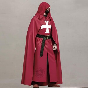Op de afbeelding: Rode cape en gewaad ensemble met capuchon. Het gewaad heeft een wit kruis embleem op de borst en een zwarte riem met een gouden gesp. De outfit heeft een lange cape en een split aan de voorkant.