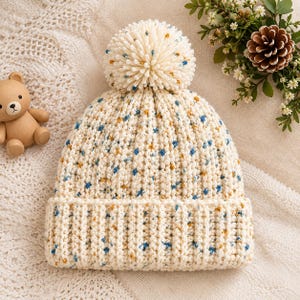 Crochet beanie pattern with pom pom featuring a textured cream crochet hat design with blue and golden accents, perfect as a crochet pom pom beanie pattern and cozy crochet winter hat pattern for handmade winter projects.