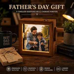 Pode incluir: Uma moldura de madeira com uma foto de pai e filho pescando, iluminada por luz quente. A moldura tem uma manivela na lateral e o texto "FATHER'S DAY GIFT" no topo. Uma caneca com "BEST DAD EVER" também é visível.