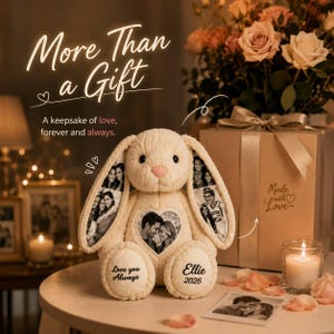 Puede incluir: Un conejo de peluche color crema con fotos impresas en sus largas orejas y un parche fotográfico en forma de corazón en el pecho. Los pies tienen bordado el texto "Love you Always" y "Ellie 2026". El conejo está junto a una caja de regalo.