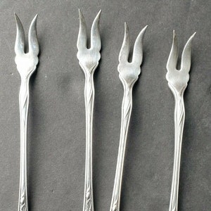 Puede incluir: Juego de cuatro tenedores de cóctel plateados con mangos ornamentados. Los tenedores tienen un diseño floral decorativo y están en excelente estado.