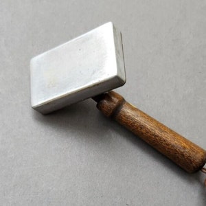 Può includere: Uno strumento di pressatura in metallo argentato con un manico in legno. Lo strumento viene utilizzato per premere il tessuto.