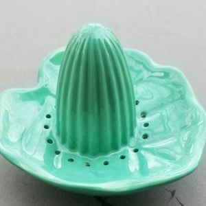 May include: A vintage green ceramic citrus juicer with a ribbed center and a leaf-shaped base.