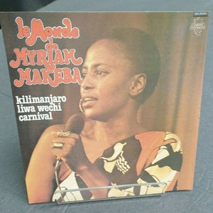 Peut inclure: Une pochette d'album vintage avec un portrait de Miriam Makeba, chanteuse, compositrice et militante sud-africaine. Le titre de l'album est "Le Monde de Miriam Makeba" et liste les chansons "Kilimanjaro", "Liwa Wechi" et "Carnival".