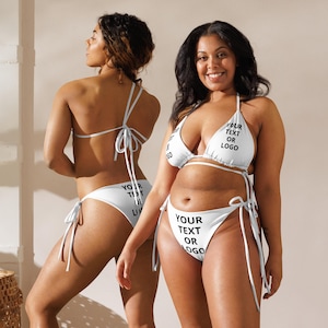 May include: White bikini with string ties. The bikini top and bottom feature the text "YOUR TEXT OR LOGO". The swimwear is designed with a triangle top and tie-side bottoms. The models are standing in front of a neutral background.