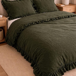 Può includere: Set di biancheria da letto verde scuro con copripiumino e due federe. La biancheria da letto ha un bordo a balze. Il letto è composto da una testiera di colore neutro e un tappeto beige.