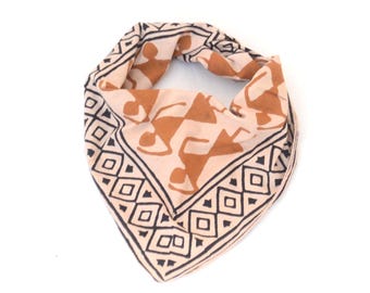 May include: A tan and brown bandana featuring a geometric border and repeating brown figures. The bandana is folded into a triangle. The fabric has a soft, slightly wrinkled appearance.