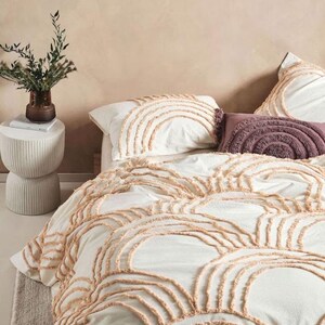 May include: White bedding set with a tufted rainbow design in a soft peach color. The set includes a duvet cover and pillowcases. A decorative purple pillow and a small side table with a vase of greenery complete the bedroom scene.