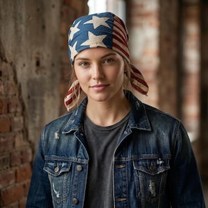 May include: A headscarf featuring a blue field with white stars and red and white stripes, styled in a classic American flag pattern. The fabric is tied at the back, and the design includes a distressed, vintage-inspired aesthetic with muted colours.