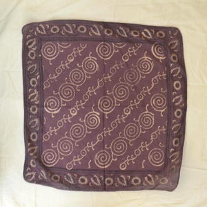 May include: A square, purple bandana with a repeating spiral and vine pattern in a lighter shade of purple. The border features a paisley and floral design. The fabric is soft and appears to be cotton.
