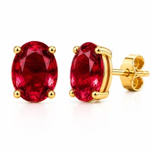 Puede incluir: Un par de pendientes de botón con piedras preciosas de color rojo intenso de corte ovalado engastadas en oro amarillo pulido. Cada piedra está asegurada por cuatro garras, mostrando el pendiente derecho el poste y el cierre de mariposa.