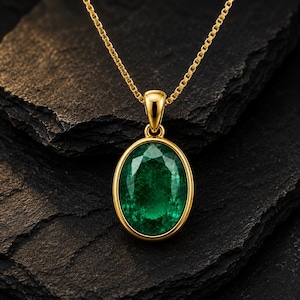 May include: A gold necklace featuring an oval-cut green gemstone pendant set in a polished gold bezel. The pendant hangs from a delicate gold box chain, showcasing a faceted surface that reflects light across the deep green stone's center.