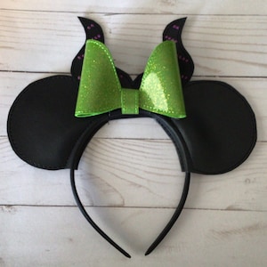May include: Black mouse ears headband with a green glitter bow and purple glitter horns.
