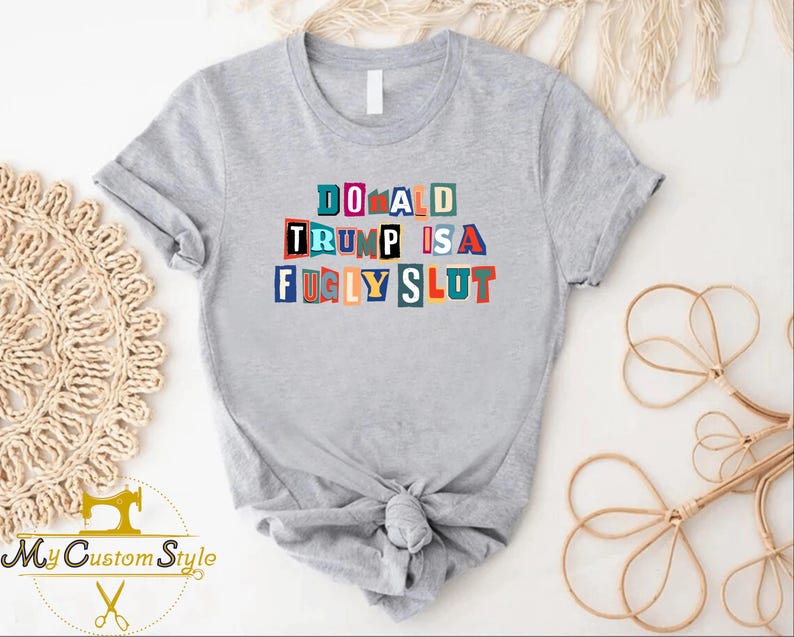 May include: A light gray t-shirt with the text "DONALD TRUMP IS A FUGLY SLUT" in colorful block letters. The shirt is knotted at the waist. The logo "My Custom Style" is visible in the lower left corner.