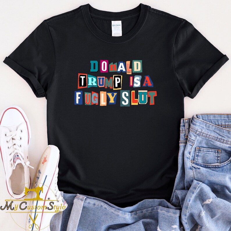 May include: Black t-shirt with the text "DONALD TRUMP IS A FUGLY SLUT" in colorful, block-letter style. The shirt is paired with blue jeans and white sneakers. The shirt is a Gildan brand.