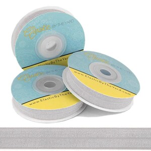 May include: Three spools of silver elastic ribbon with the text "Elastic By The Yard" and the website address "www.ElasticByTheYard.com" printed on the labels.